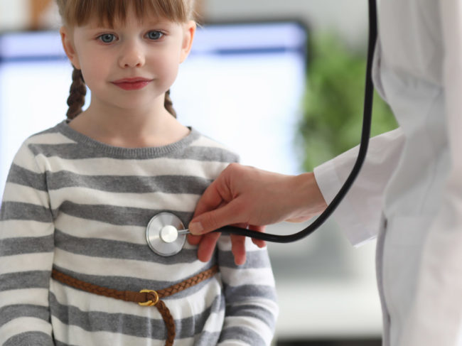 Doctor with stethoscope listening to heart of girl